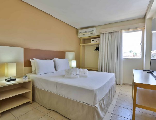 Aconchegante quarto com uma cama de casal no Thermas de Olímpia Resorts by Mercure. Janela para iluminar o ambiente com luz natural e permitir uma vista relaxante. Mesa de cabeceira ao lado da cama, equipada com uma suave luz de leitura para momentos tranquilos. TV a cabo disponível para entretenimento dos hóspedes. Roupas de cama inclusas para uma estadia confortável e sem preocupações.