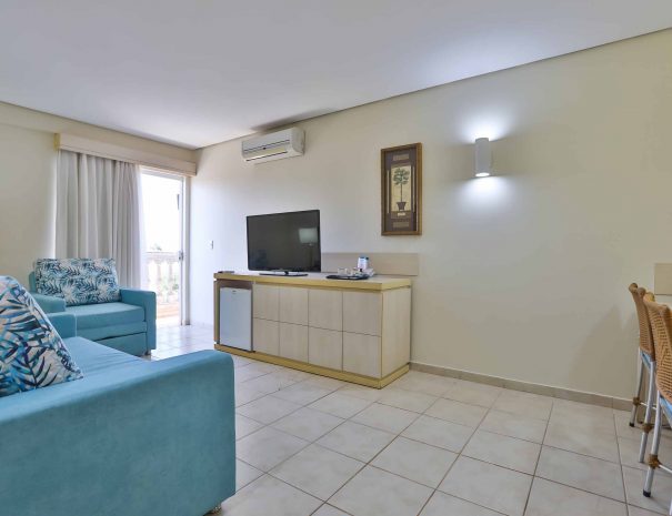 Espaçosa sala de estar da Suíte Master no Thermas de Olímpia Resorts by Mercure. Decoração elegante com sofá e poltrona em tons acolhedores. Frigobar para uso livre e TV a cabo disponível para os hóspedes. Ambiente naturalmente refrigerado e com ar-condicionado. Móvel de organização e mesa para comodidade dos visitantes. O refúgio perfeito para relaxar e desfrutar de momentos memoráveis durante a estadia.