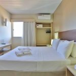 Piso Superior: Suíte principal com cama de casal e decoração elegante, iluminada por uma janela. Conte também com um banheiro exclusivo da Suíte.