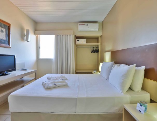 Piso Superior: Suíte principal com cama de casal e decoração elegante, iluminada por uma janela. Conte também com um banheiro exclusivo da Suíte.